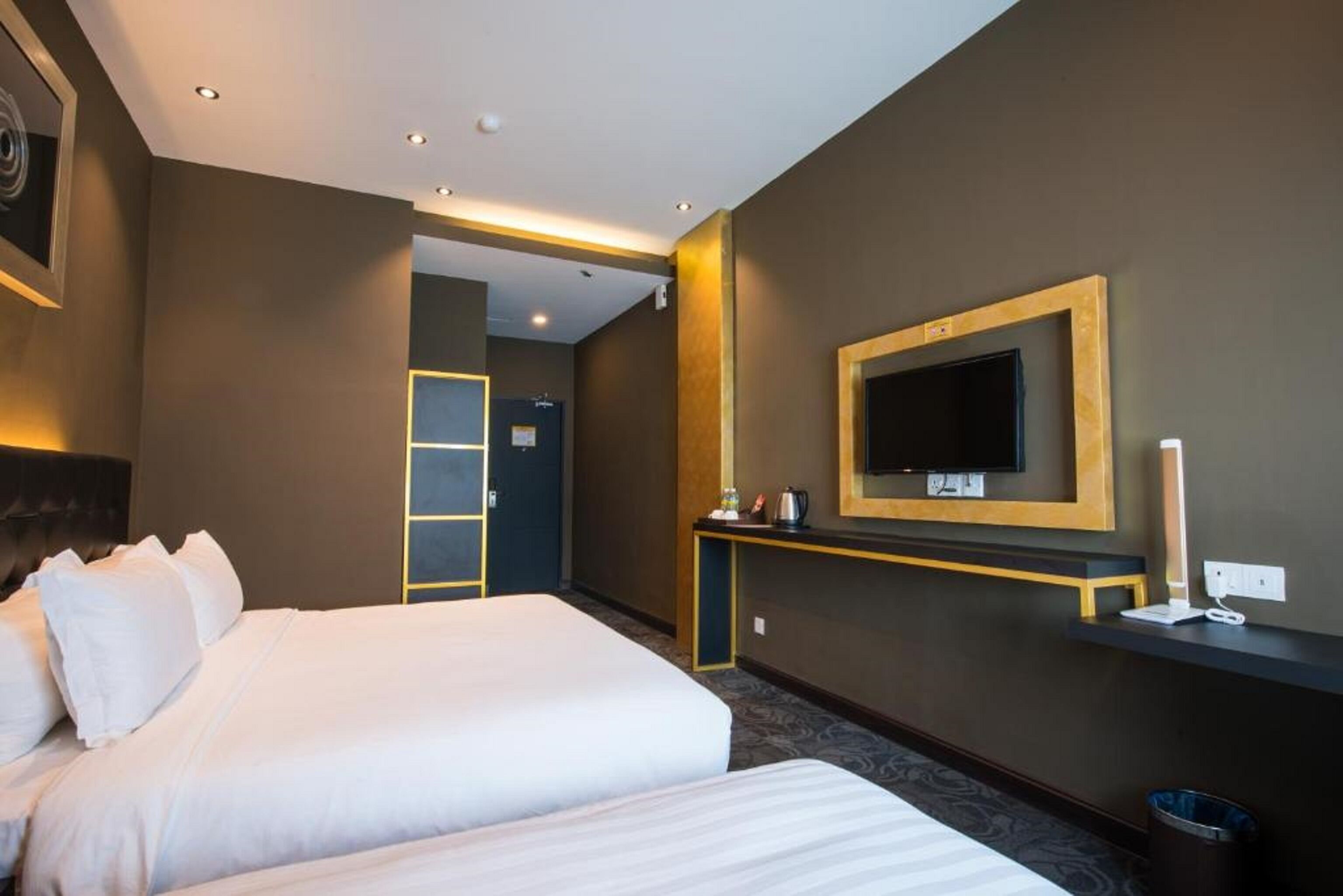 Une chambre d’hôtel avec deux lits, un téléviseur fixé au mur, une table de chevet et un petit bureau avec une lampe.