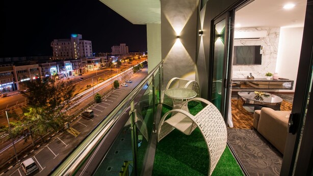 A balcony with a view of a city street at night, a glass door leading to a modern interior with a sofa and a round table. - Asiatic Hotel (Malacca City)