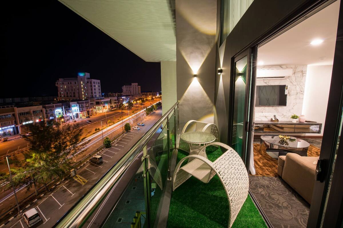 A balcony with a view of a city street at night, a glass door leading to a modern interior with a sofa and a round table.