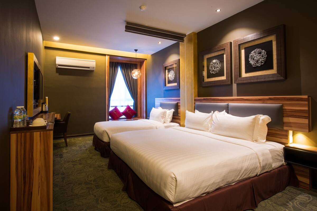 A hotel room with two beds, a desk with a chair, an air conditioner, and framed artwork on the wall.