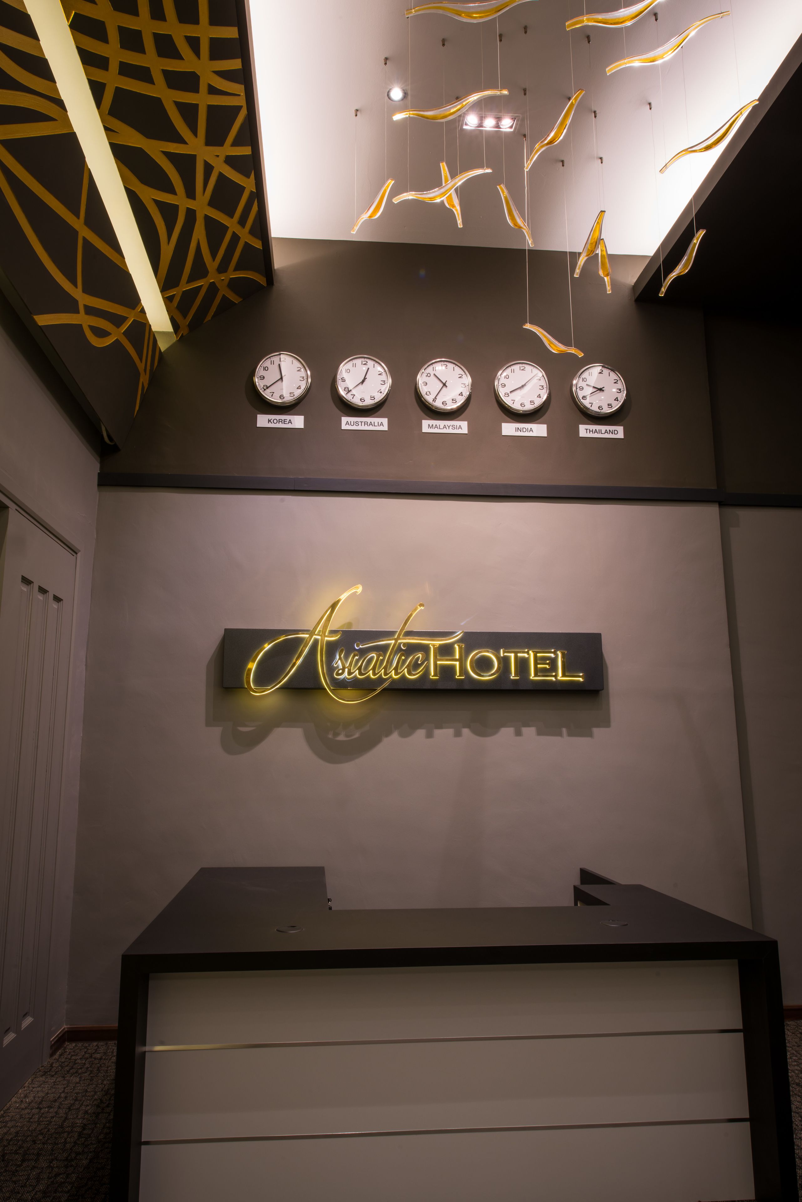 A reception desk with a neon sign reading "Asiatic Hotel" and clocks displaying times from various countries.