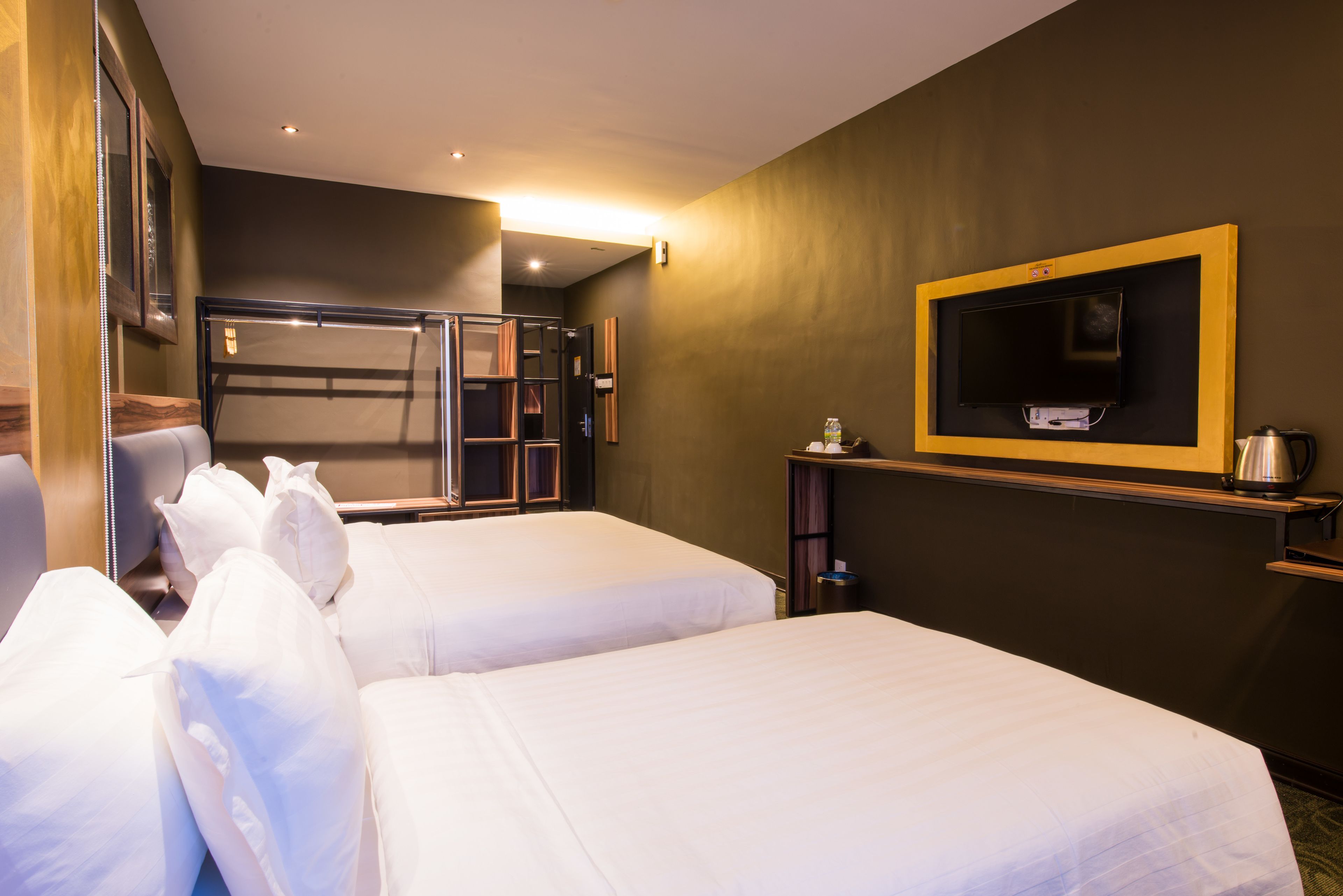 A hotel room with two beds, a TV mounted on the wall, and a small table with a kettle.
