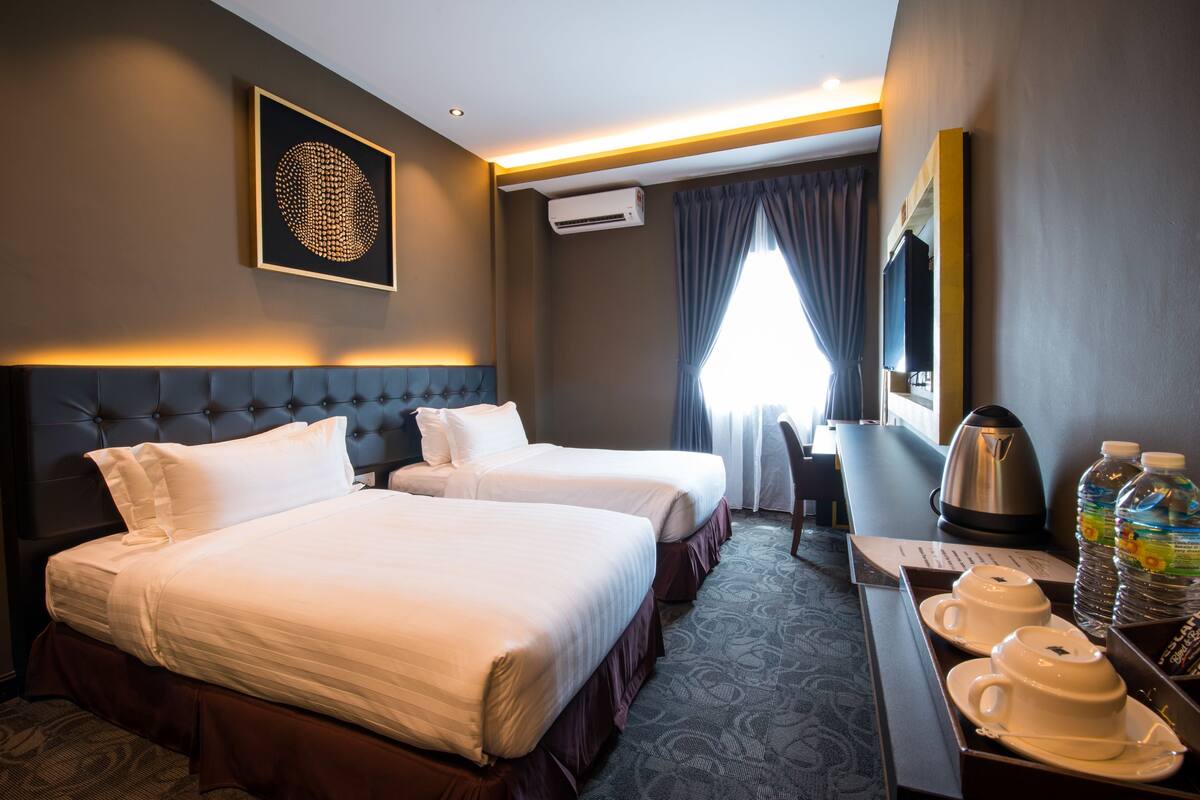 A hotel room with two beds, a coffee maker, a kettle, and a tray with cups and a water bottle.