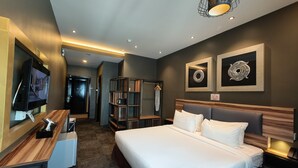 A modern hotel room with a large bed, a TV, a desk, and a wardrobe. - Asiatic Hotel (Malacca City)