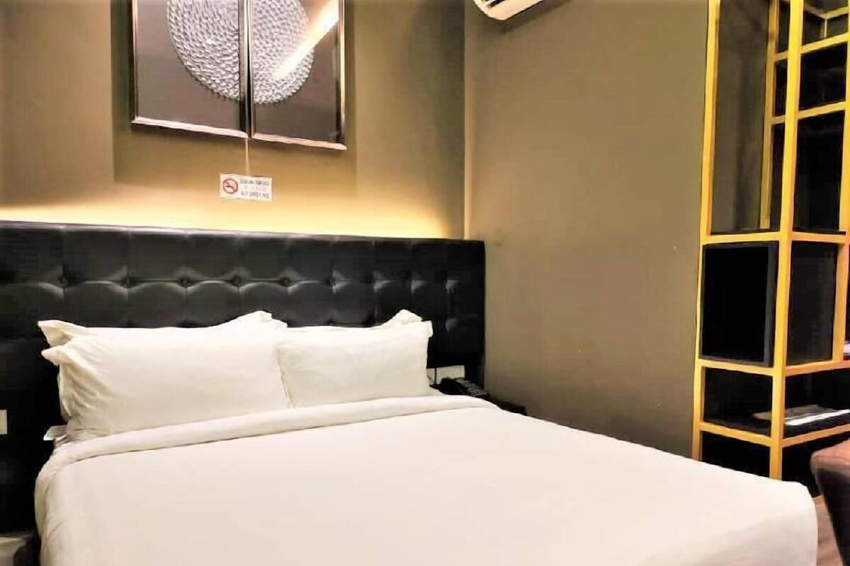 A neatly made bed with white linens, a tufted headboard, and a wall-mounted round mirror.
