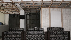 Une pièce avec trois canapés à motifs, des poutres en bois au plafond, un mur recouvert de carreaux et un meuble noir.