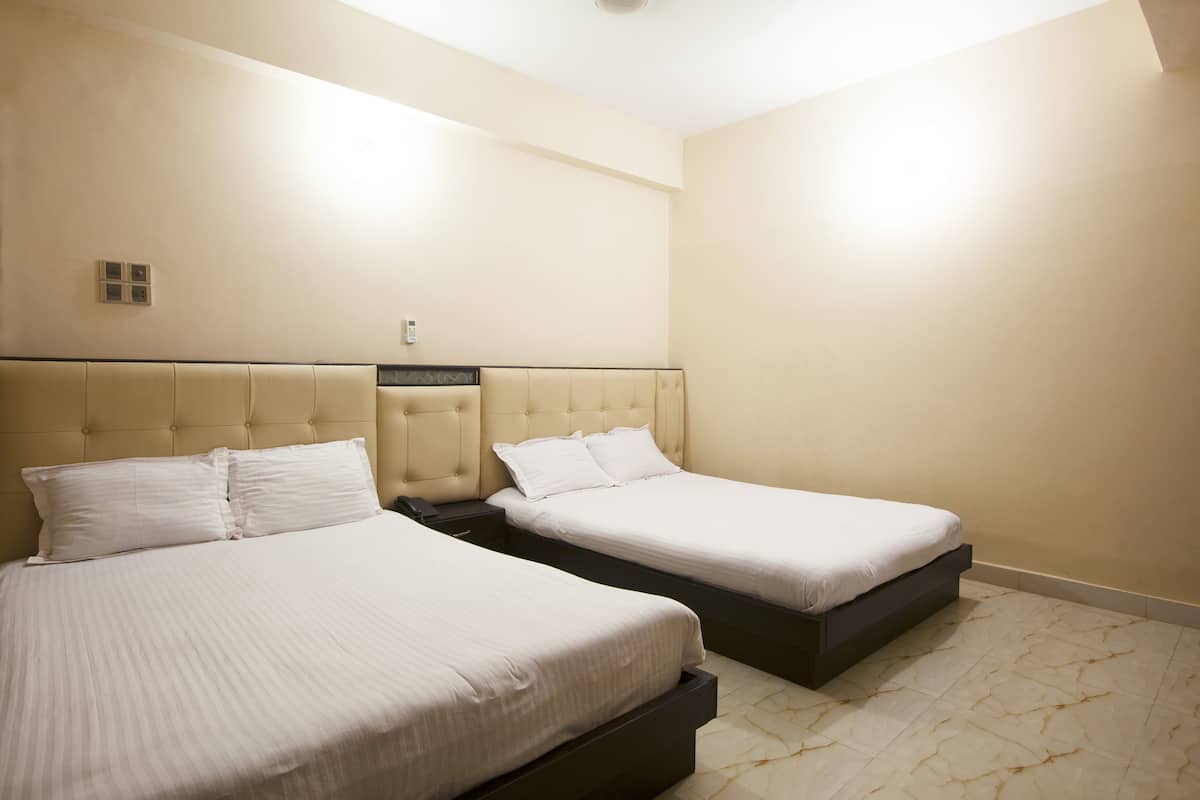 A hotel room with two beds, a nightstand, and a wall-mounted light fixture.