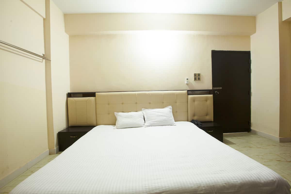 A hotel room with a large bed, two bedside tables, a headboard, and a door.