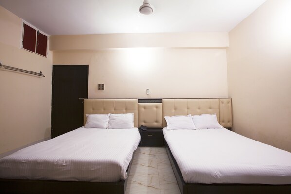 Une chambre d’hôtel avec deux lits simples, une petite table de chevet, un radiateur fixé au mur et une porte.