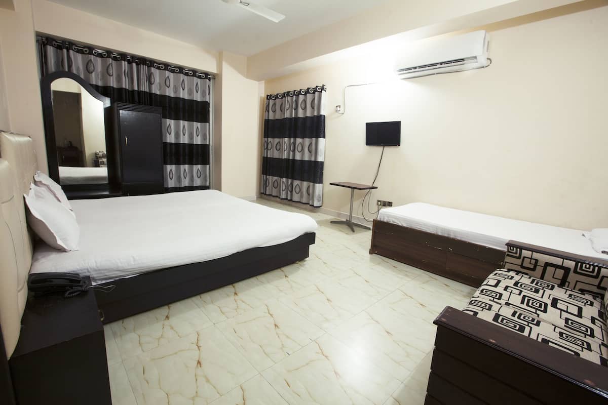 A bedroom with a bed, a bedside table, a dresser, a mirror, curtains, and an air conditioning unit.