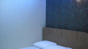 Ein Einzelbett mit Holz Kopfteil und weißer Bettwäsche in einem Zimmer mit Wandtapete mit Muster.