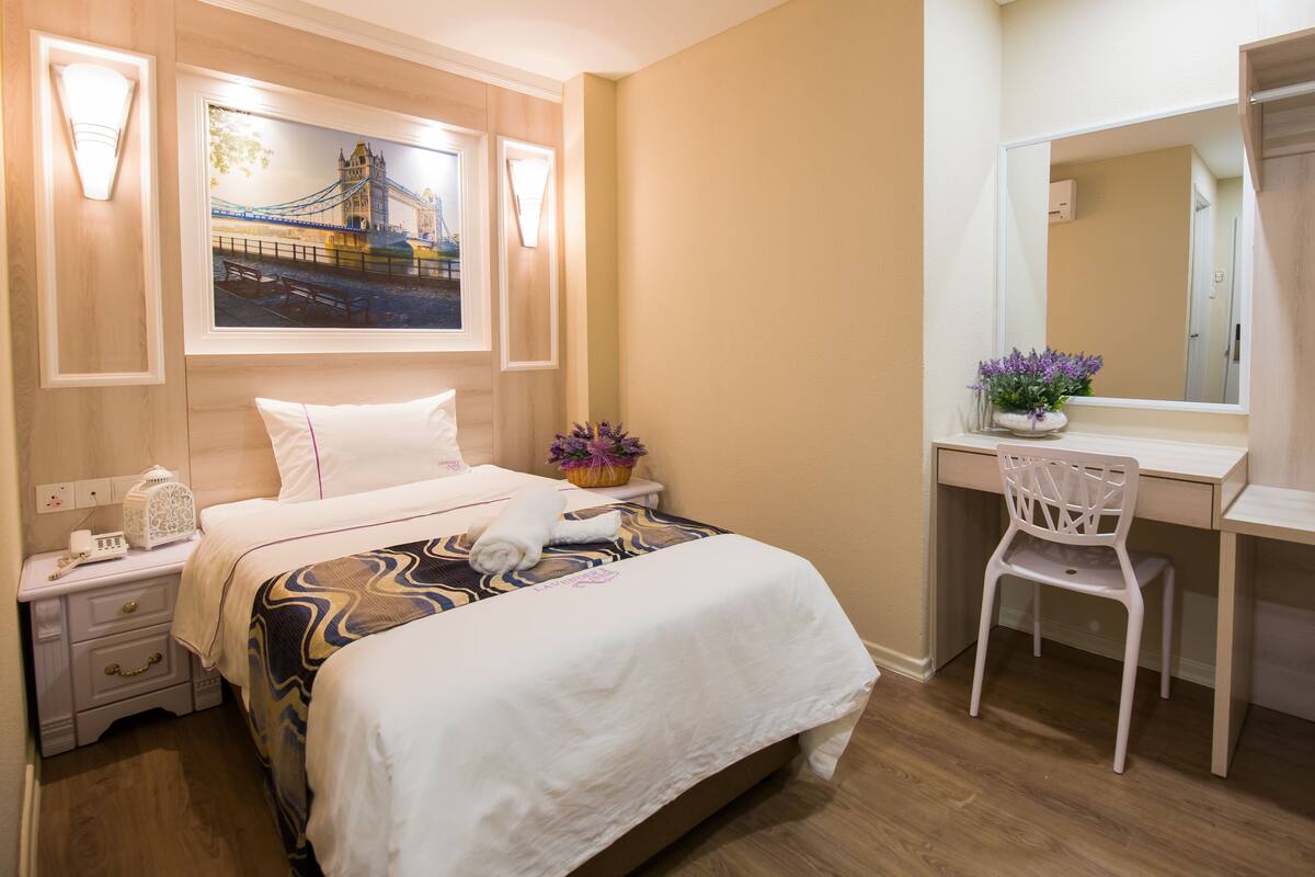 A hotel room with a bed, bedside table, lamp, and a desk with a chair.