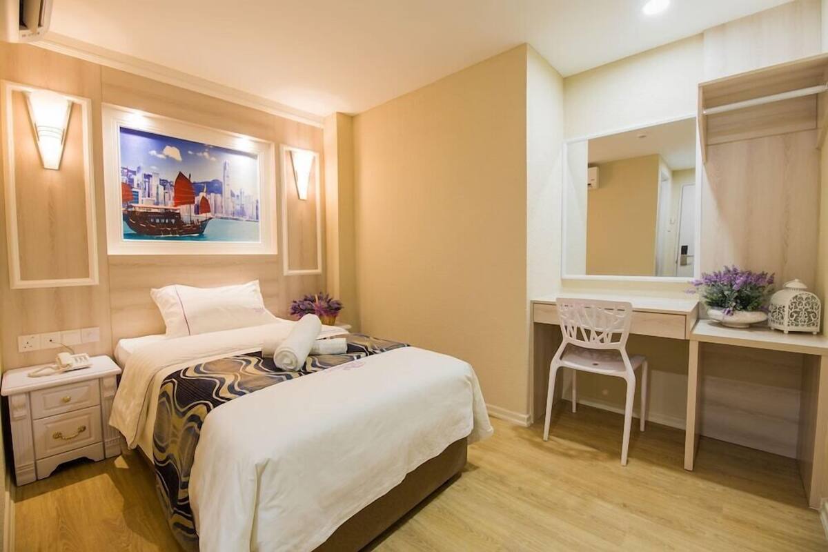 A hotel room with a bed, bedside table, desk, chair, and a large mirror.