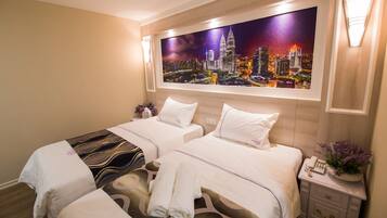 A hotel room with two beds, a nightstand with a phone and a vase of flowers, and a cityscape painting above the beds.