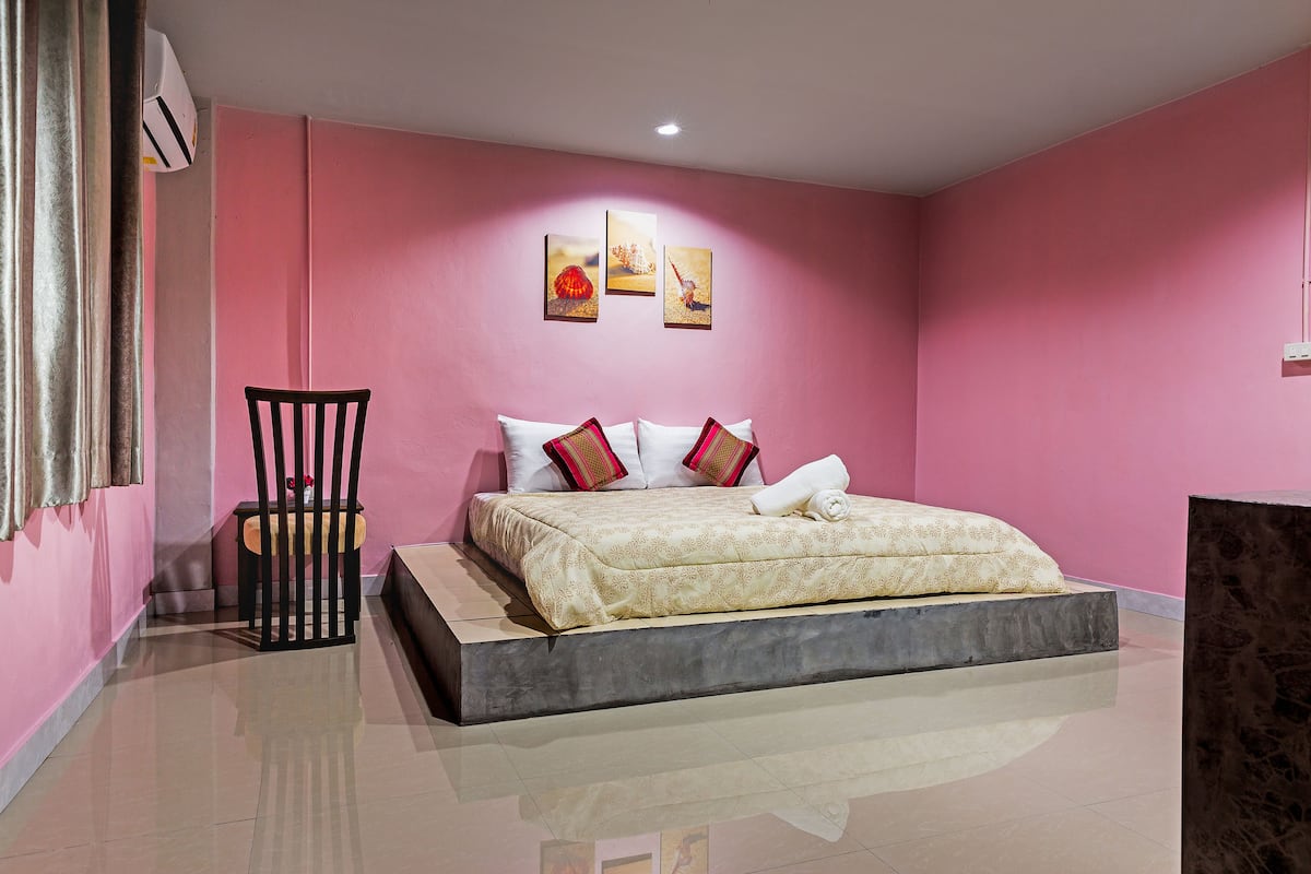 Un dormitorio con una cama, una silla, una mesita y aire acondicionado de pared.
