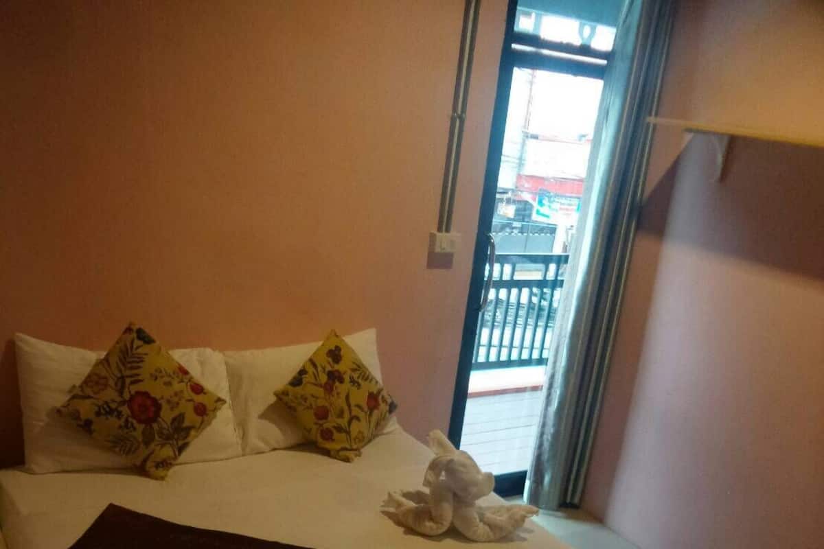 Una cama bien hecha con almohadones florales, un edredón oscuro y dos toallas blancas.