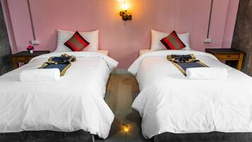 A hotel room with two beds, each with white bedding and red and black pillows. There is a wall-mounted light fixture above the beds, and a small table with a vase of flowers on one side.
