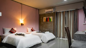 A hotel room with two beds, a desk, and a chair. There is a window with curtains and an air conditioning unit on the wall. - The Guest Hotel - Hostel (Krabi)