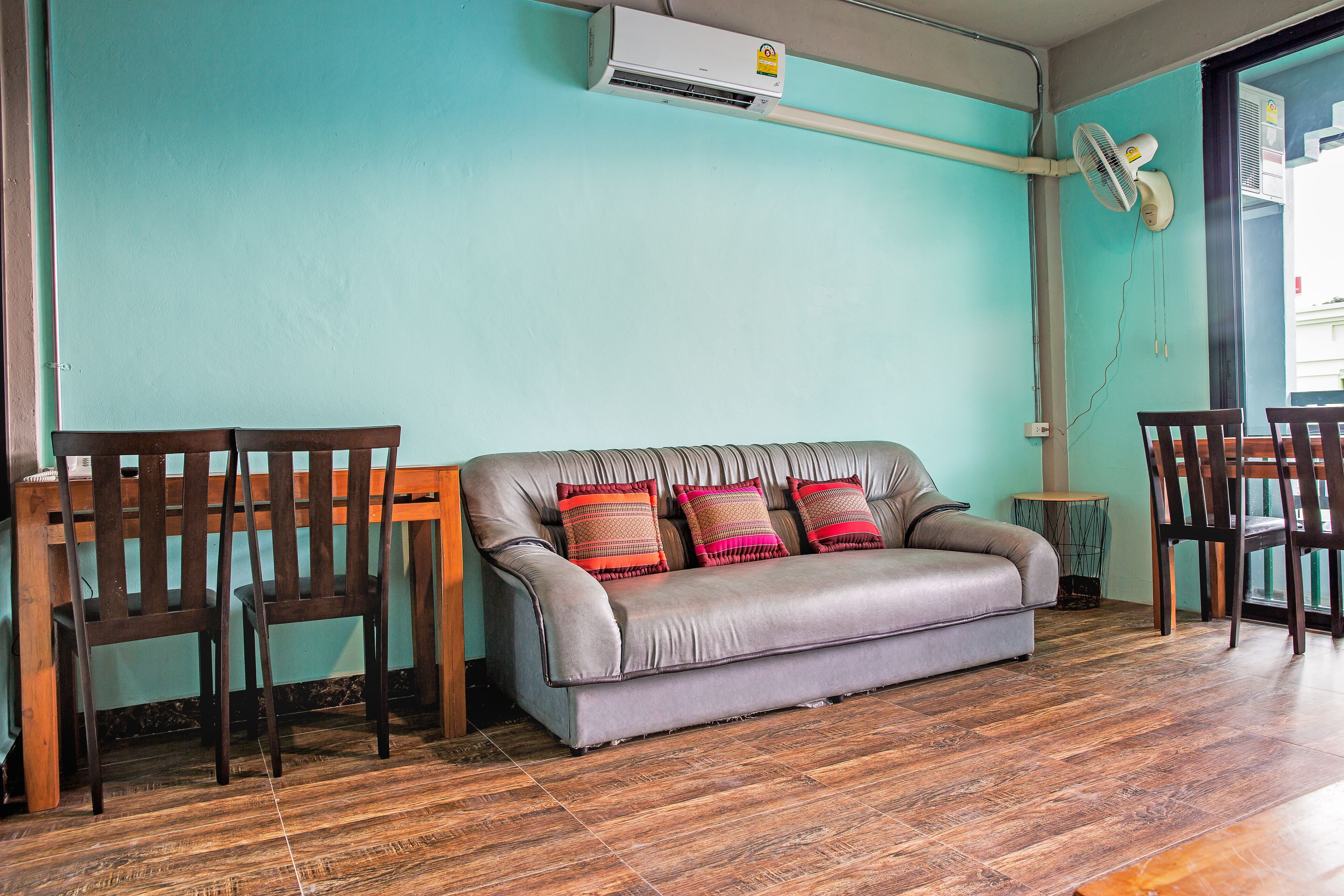 Una habitación con un sofá gris, dos sillas de madera, una mesita redonda y un equipo de aire acondicionado en la pared.
