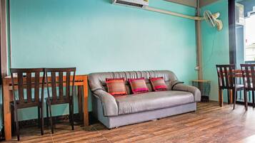 Una habitación con un sofá gris, dos sillas de madera, una mesita redonda y un equipo de aire acondicionado en la pared.