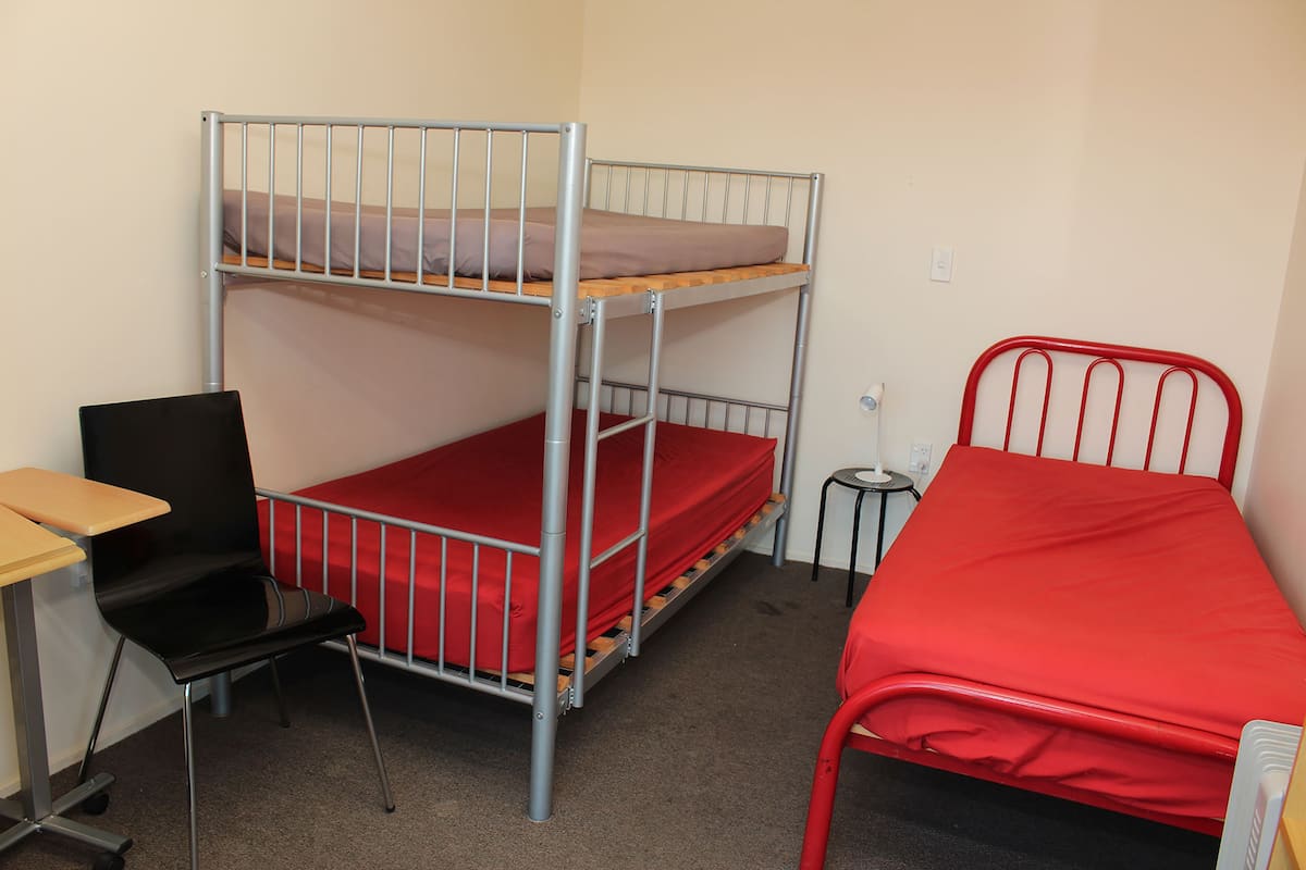 A bunk bed with a desk and chair, a small table, and a red mattress.