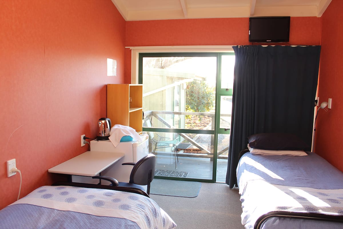 A room with two beds, a desk, a chair, a television, and a window with curtains.