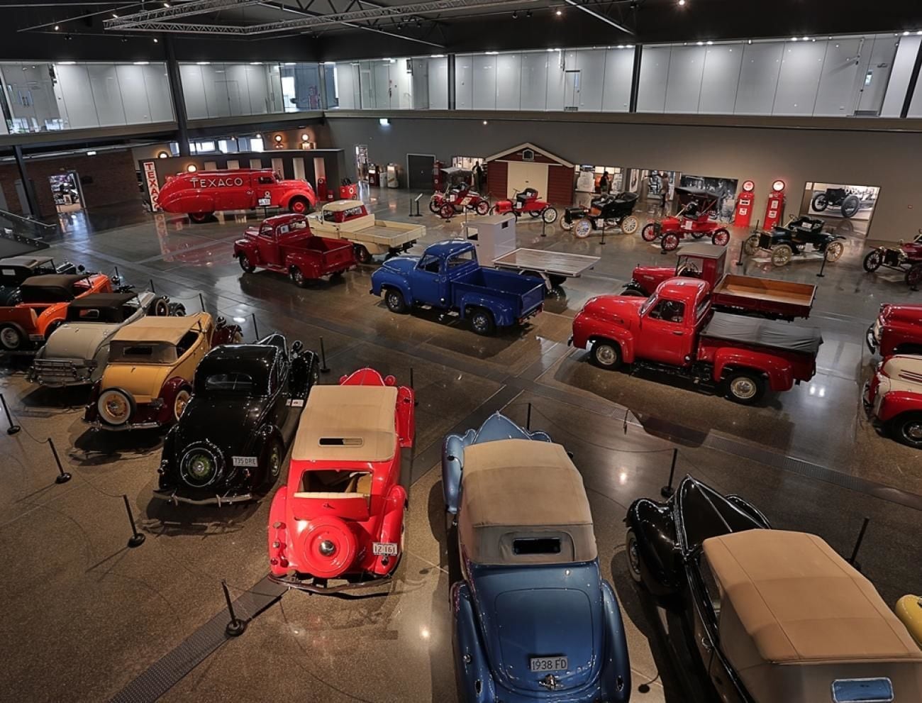 A museum with various vintage cars on display, including a red Texaco truck and a blue truck.
