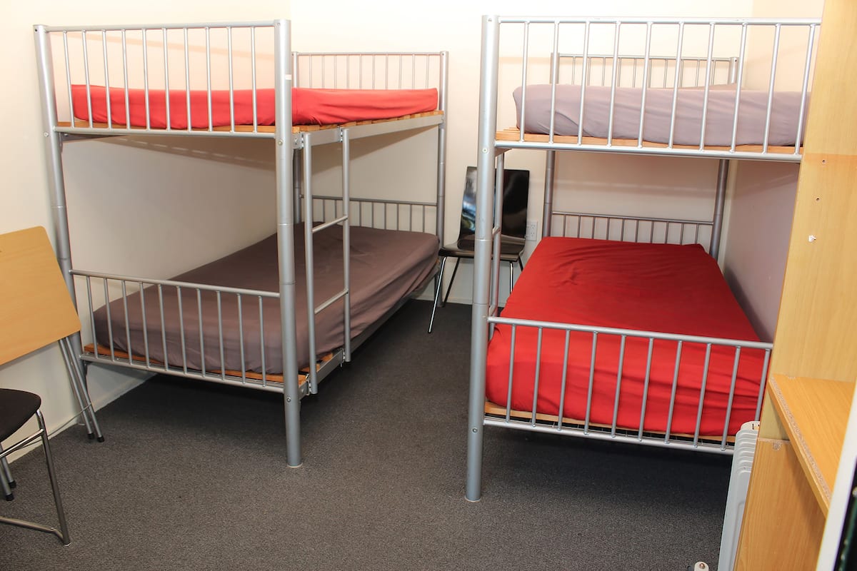 A bunk bed room with two bunk beds, each with a mattress and pillows. There is a desk and a chair in the room.