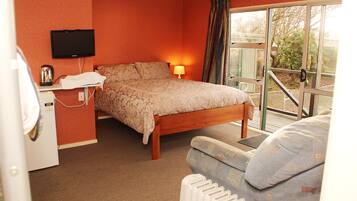 A bedroom with a bed, a bedside table with a lamp, a television on the wall, and a window with curtains.