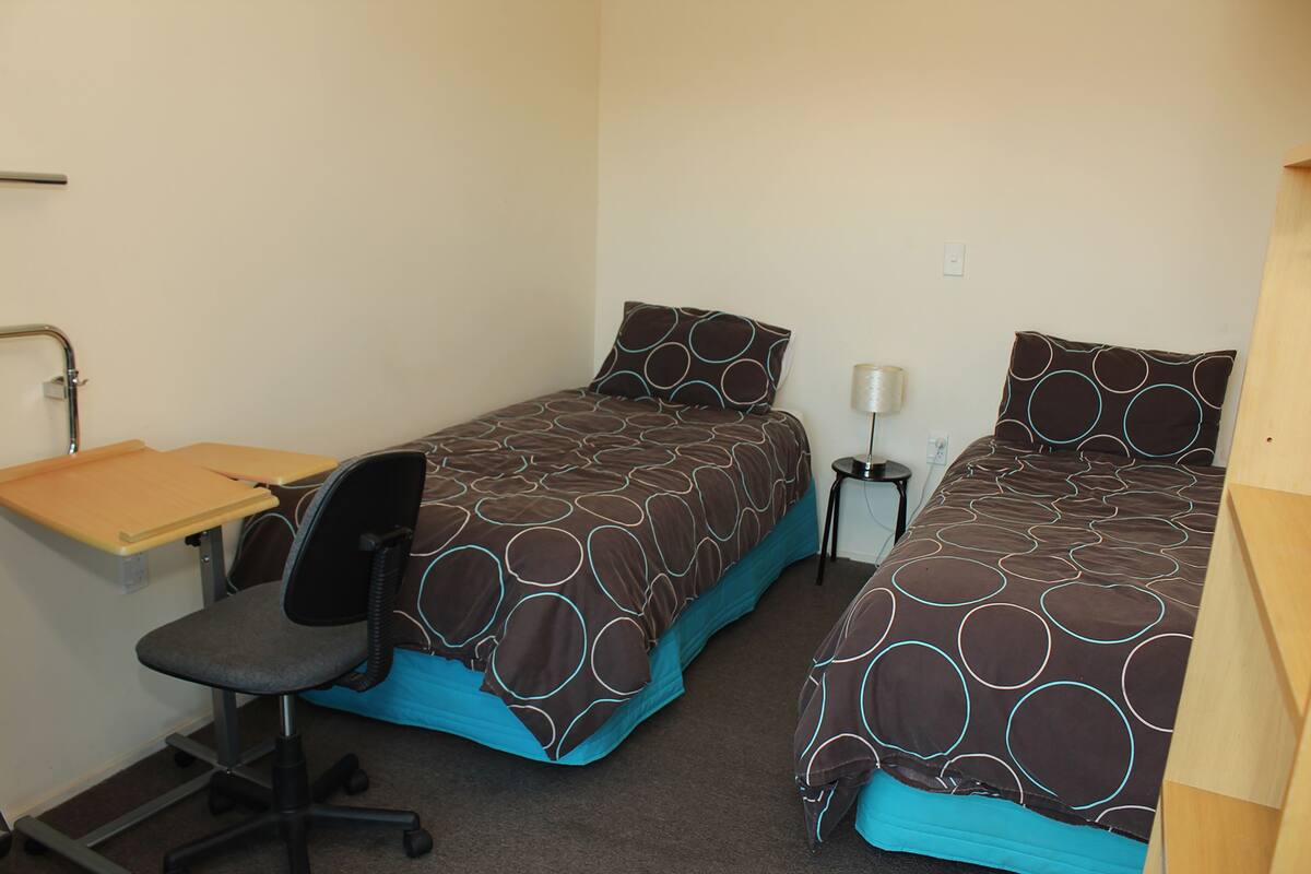 A room with two single beds, a desk, and a chair.