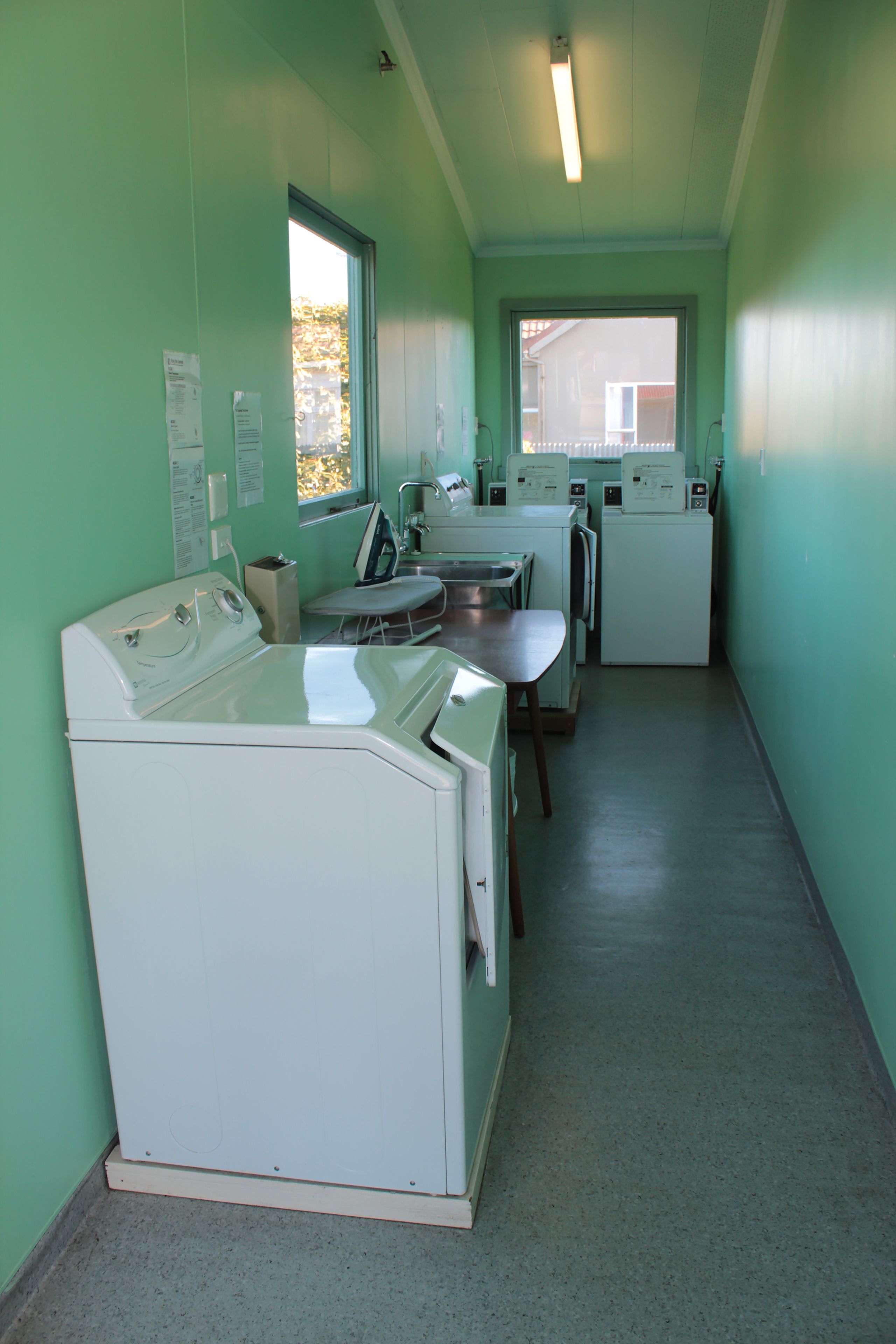 A laundry room with a washing machine, dryer, ironing board, and a sink.