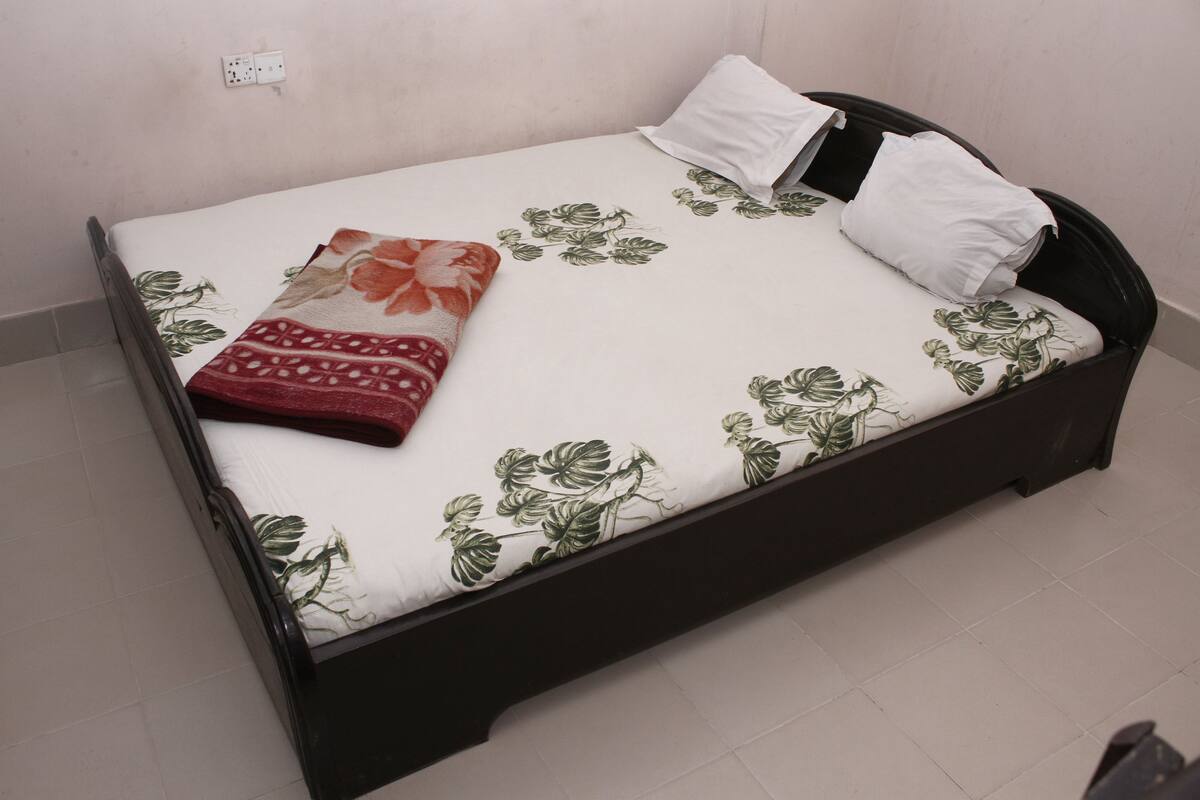 Een bed met een bloemenbedekking, een rode plaid en twee kussens.