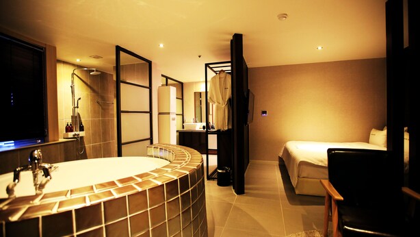 A modern hotel room with a large bathtub, a bed, a chair, and a television. - Hotel The Ann (Changwon)