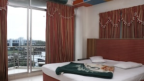 A hotel room with a large bed, a window with curtains, and a view of buildings outside. - White Beach Hotel (Cox's Bazar)