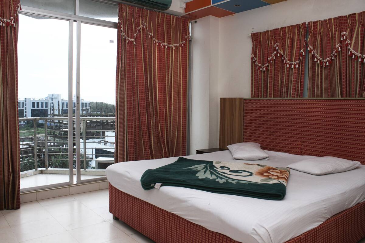Une chambre d’hôtel avec un grand lit, une fenêtre avec des rideaux et une vue sur les bâtiments environnants.