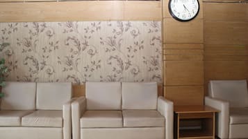 A reception area with a wooden panel wall, a floral wallpaper design, and a clock. There are two sofas and a small wooden table.