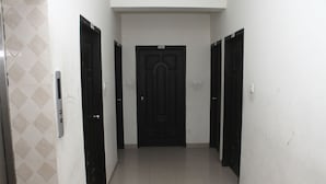 A hallway with a black door at the end, white walls, and a tiled floor. - White Beach Hotel (Cox's Bazar)