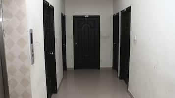 A hallway with a black door at the end, white walls, and a tiled floor.