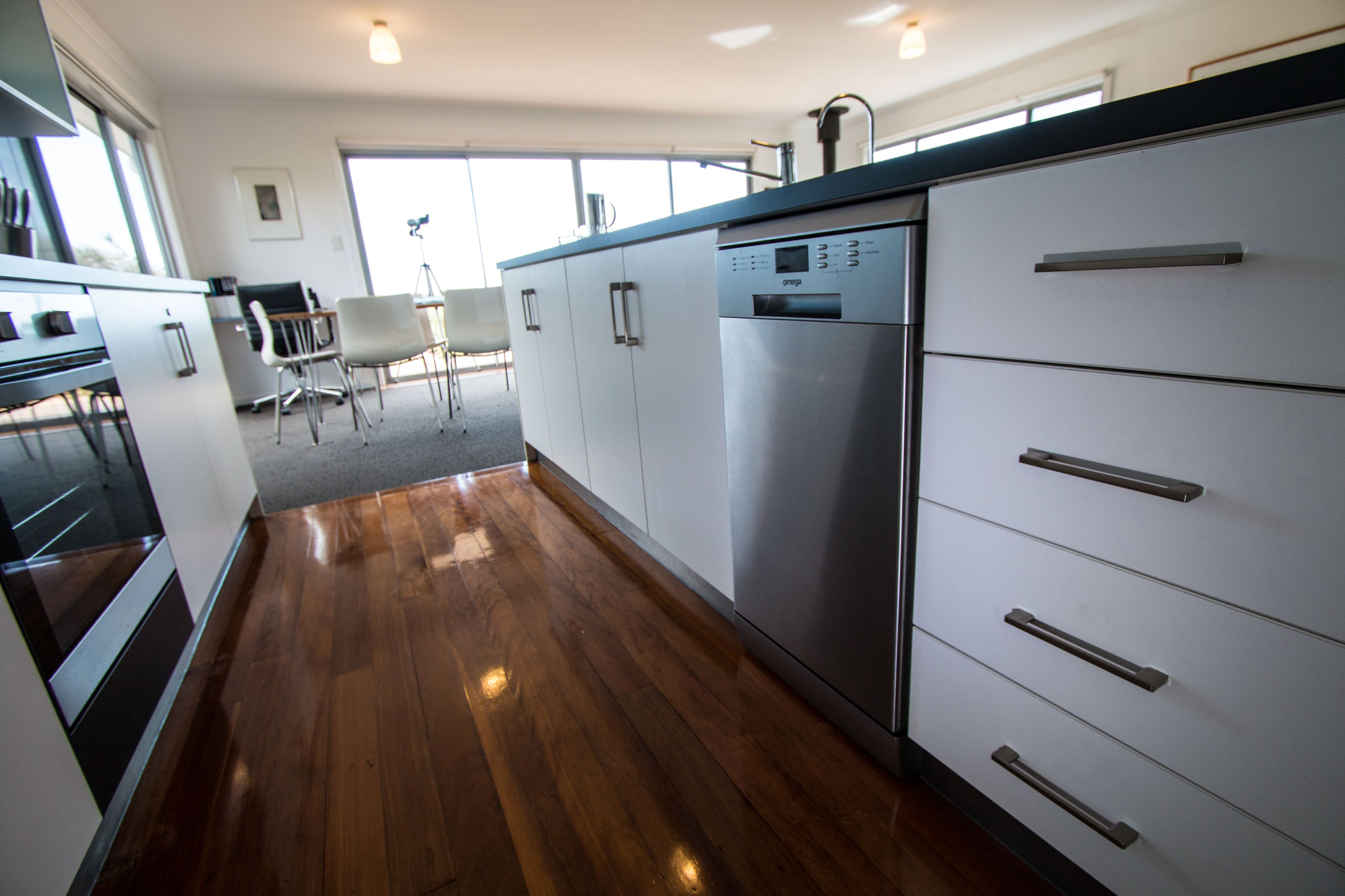 A modern kitchen with stainless steel appliances, wooden flooring, and white cabinetry.