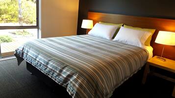 Habitación de hotel con una cama grande, dos lámparas de noche y un ventanal con vistas a árboles.