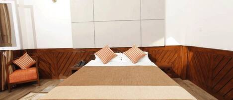 A hotel room with a large bed, wooden paneling on the walls, a chair, and a wall-mounted light fixture.