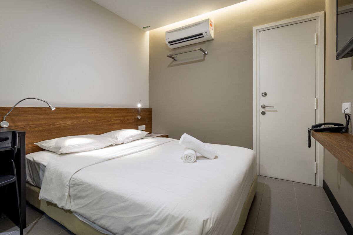 Een hotelkamer met een bed, nachtkastje, lamp, airconditioning en een deur.