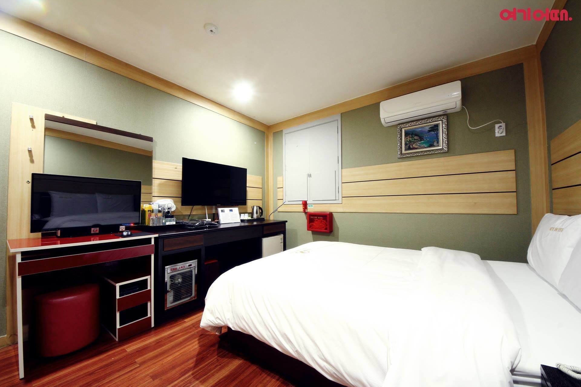 A hotel room with a bed, a desk with a computer, a television, and a wall-mounted air conditioner.