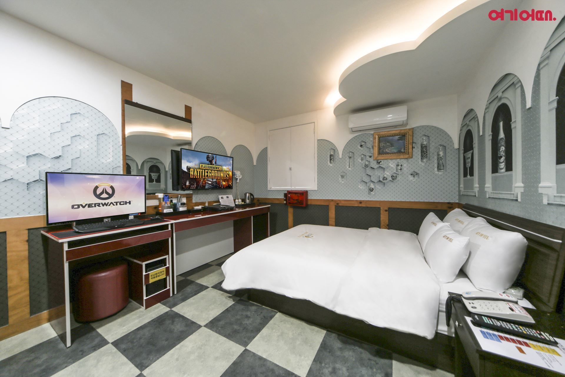 Een hotelkamer met een bed, een bureau met een computer, een televisie en een muur met decoratieve elementen.