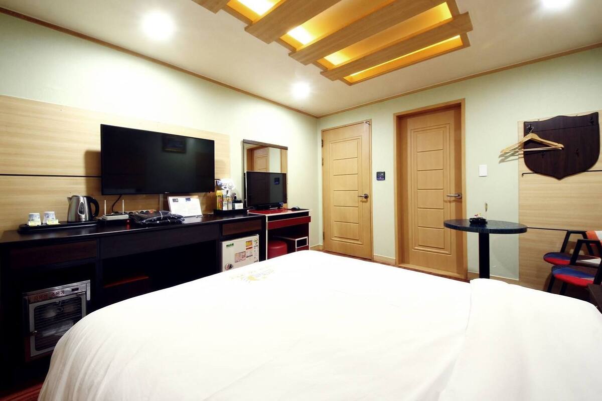 A hotel room with a bed, a desk with a television, a mirror, and a wardrobe.