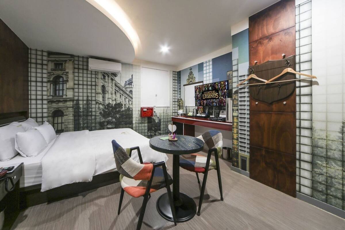 A hotel room with a bed, a round table with chairs, a bar area, and a large window.