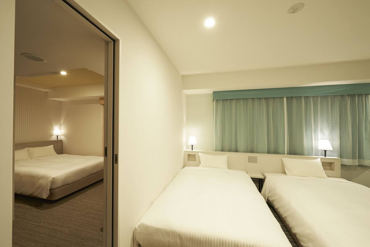 Ein Hotelzimmer mit zwei Betten, einem großen Spiegel und einem Fenster mit Vorhängen.