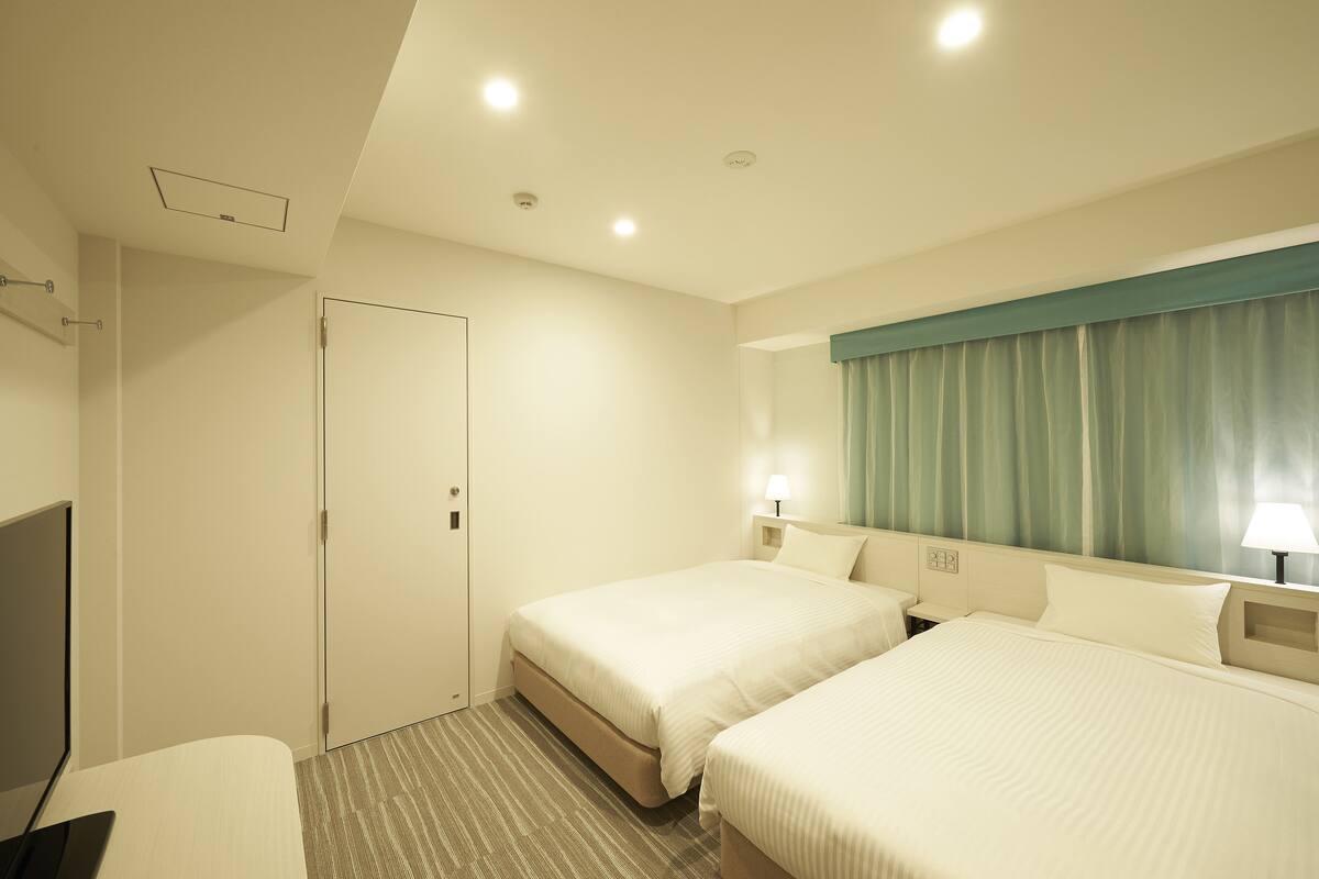 Ein Hotelzimmer mit zwei Betten, einem Schreibtisch, einem Fernseher und einer Badezimmertür.