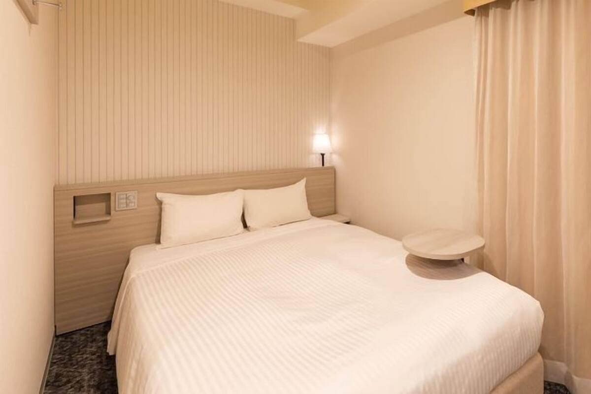 Ein Hotelzimmer mit einem Bett, einem Nachttisch, einer Wandleuchte und einem Fenster mit Vorhängen.