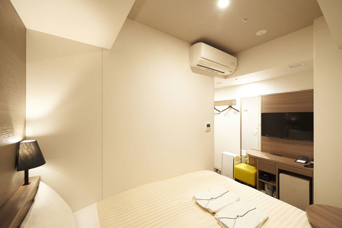 Ein Hotelzimmer mit Bett, Nachttisch, Lampe, Klimaanlage, Fernseher und Spiegel.